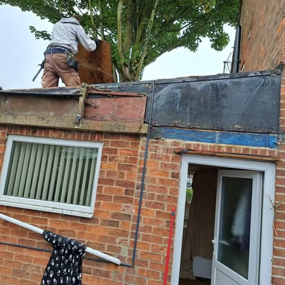 Worker stripping old flat roof on brick house extension
