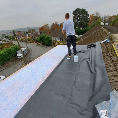 Roofer laying EPDM membrane on sloped roof