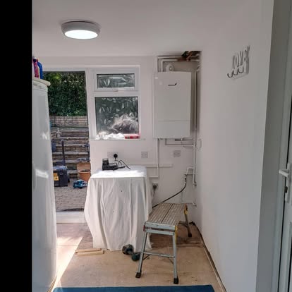 Utility room with boiler on wall and bare floor