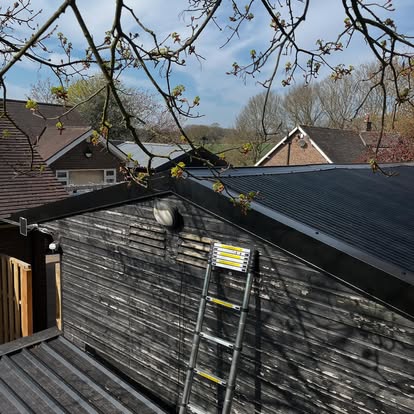Black corrugated metal roof on dark timber barn with ladder
