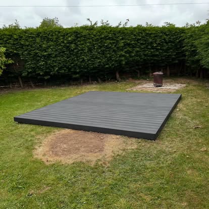 Grey composite flat deck in garden with hedgerow