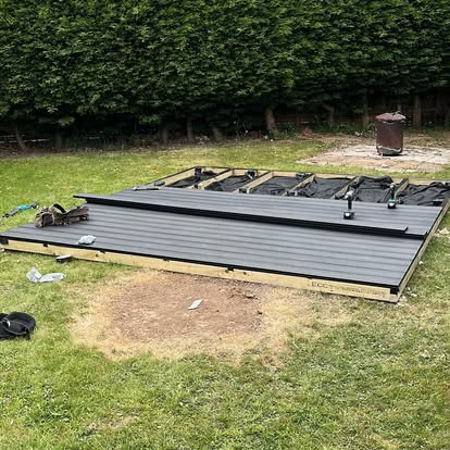 Grey composite deck being installed in hedge garden
