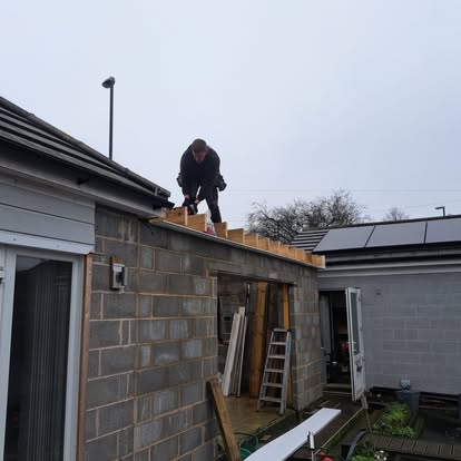 Worker fixing roof timbers on block wall extension